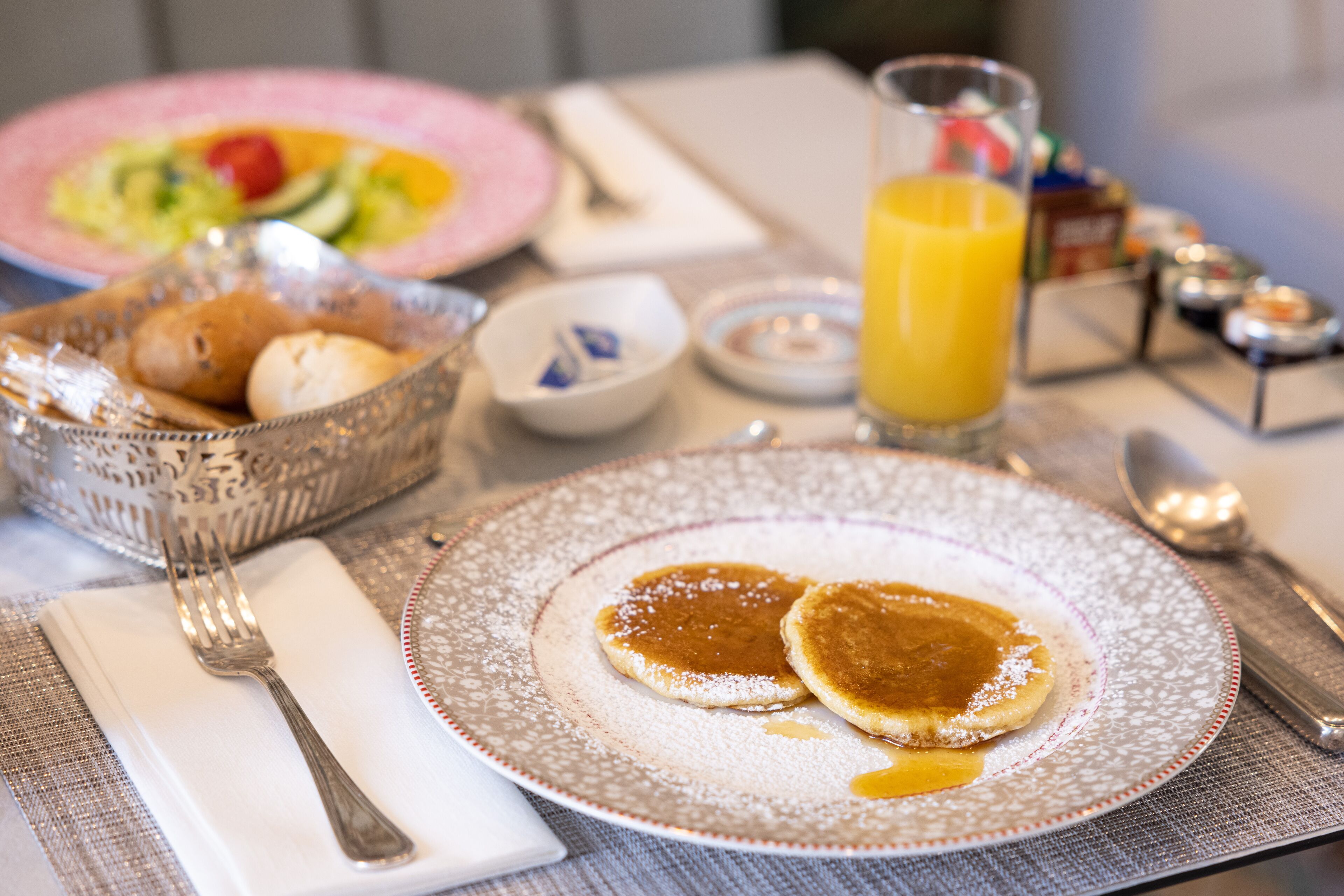 Ein Frühstückstisch mit Pfannkuchen, einem Glas Orangensaft und verschiedenen Frühstücksleckereien.