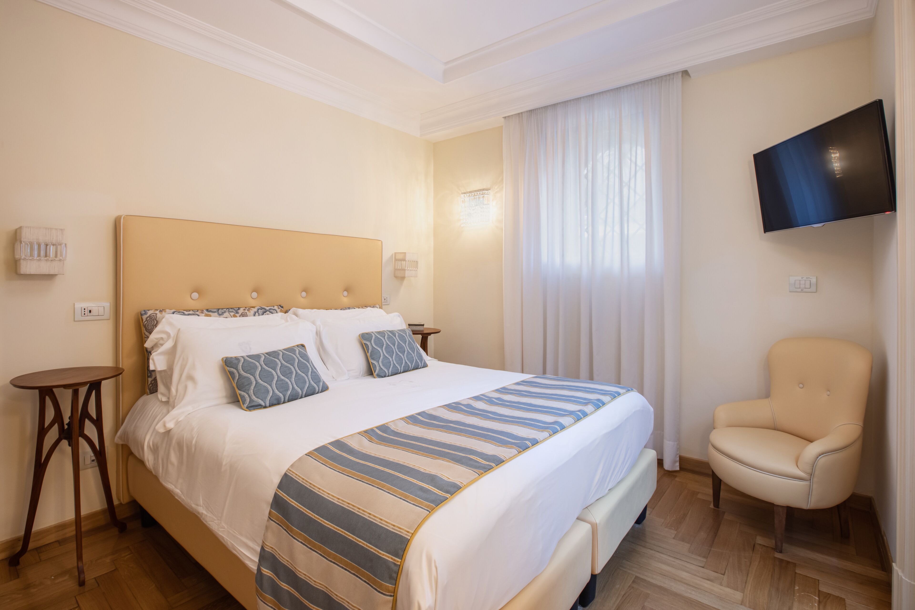 Una camera d'albergo con un letto grande, una sedia, una TV a schermo piatto e una finestra con tende.