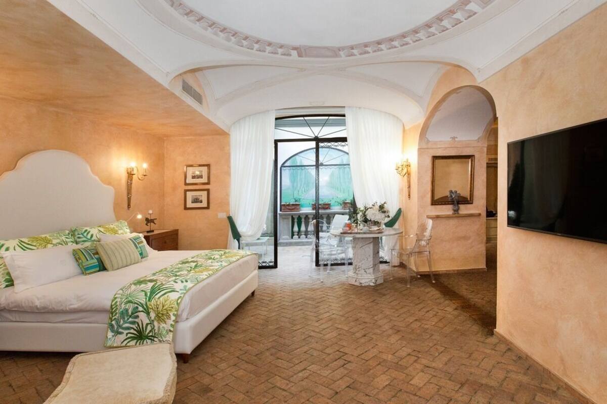 A spacious bedroom with a large bed, a television, and a balcony with a view.