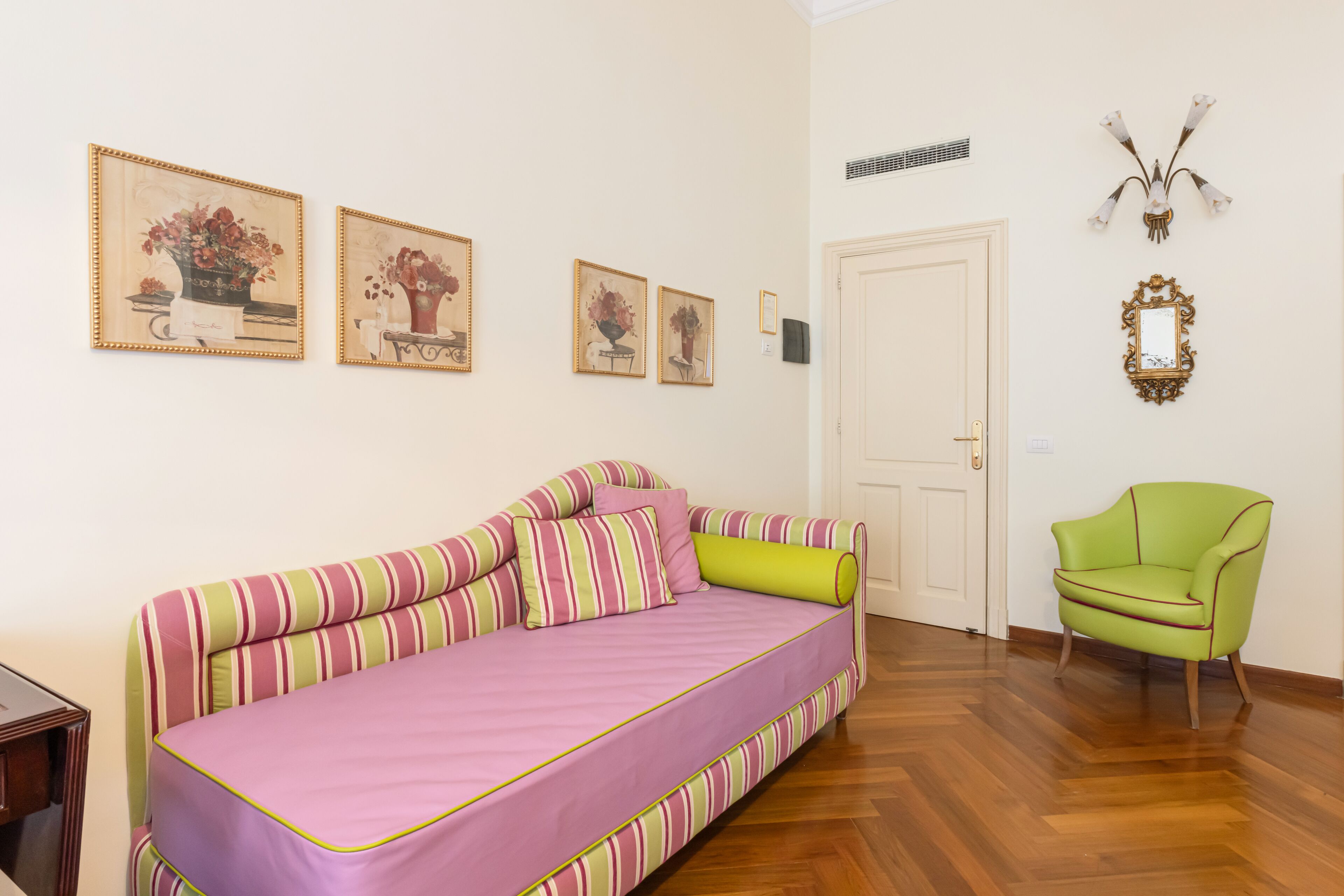 Una habitación con un sofá a rayas, un sillón verde y cuadros con motivos florales en la pared.