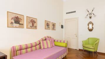 Una habitación con un sofá a rayas, un sillón verde y cuadros con motivos florales en la pared.