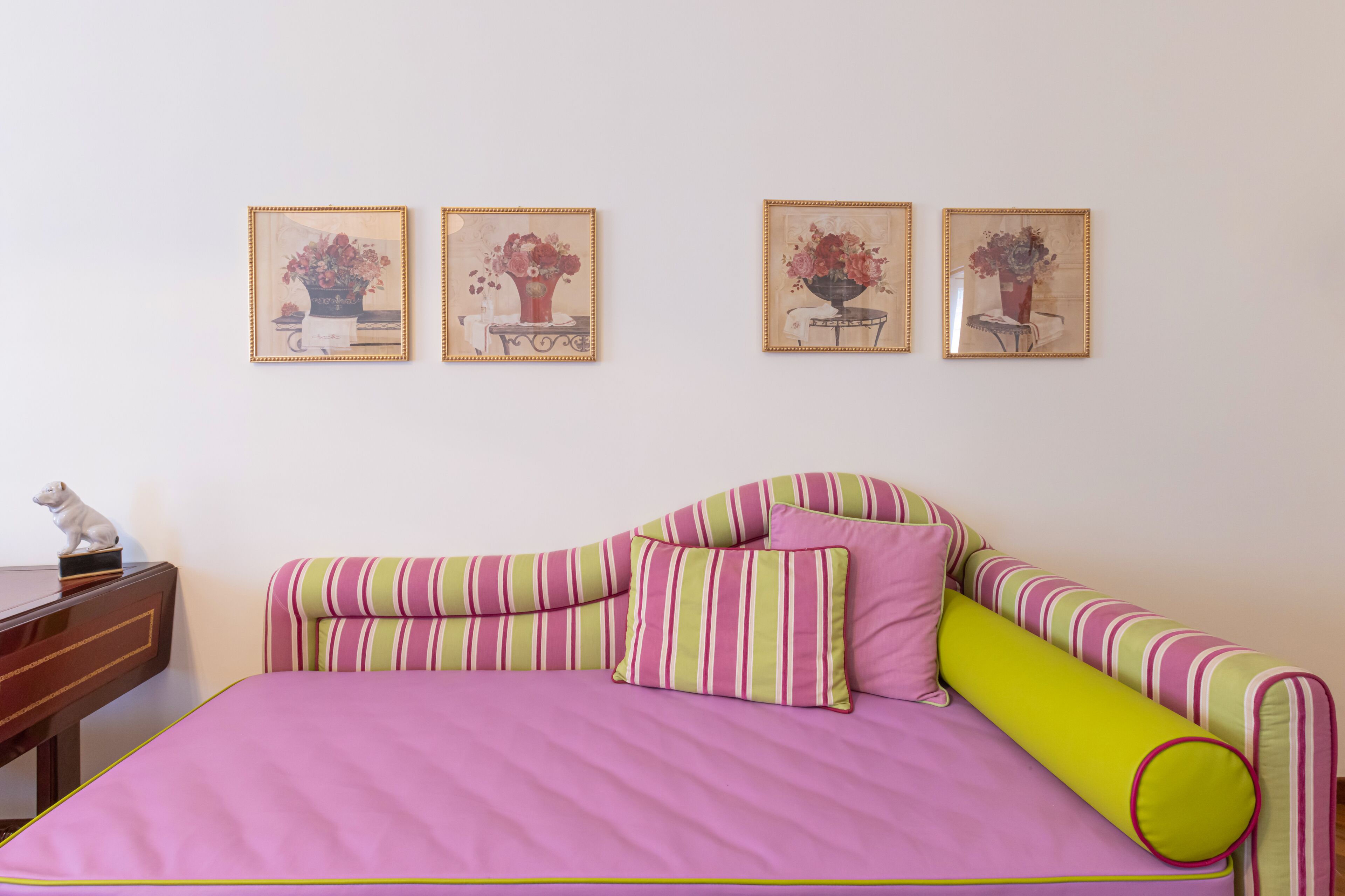 A room with a bed, a desk, and four framed floral paintings on the wall.