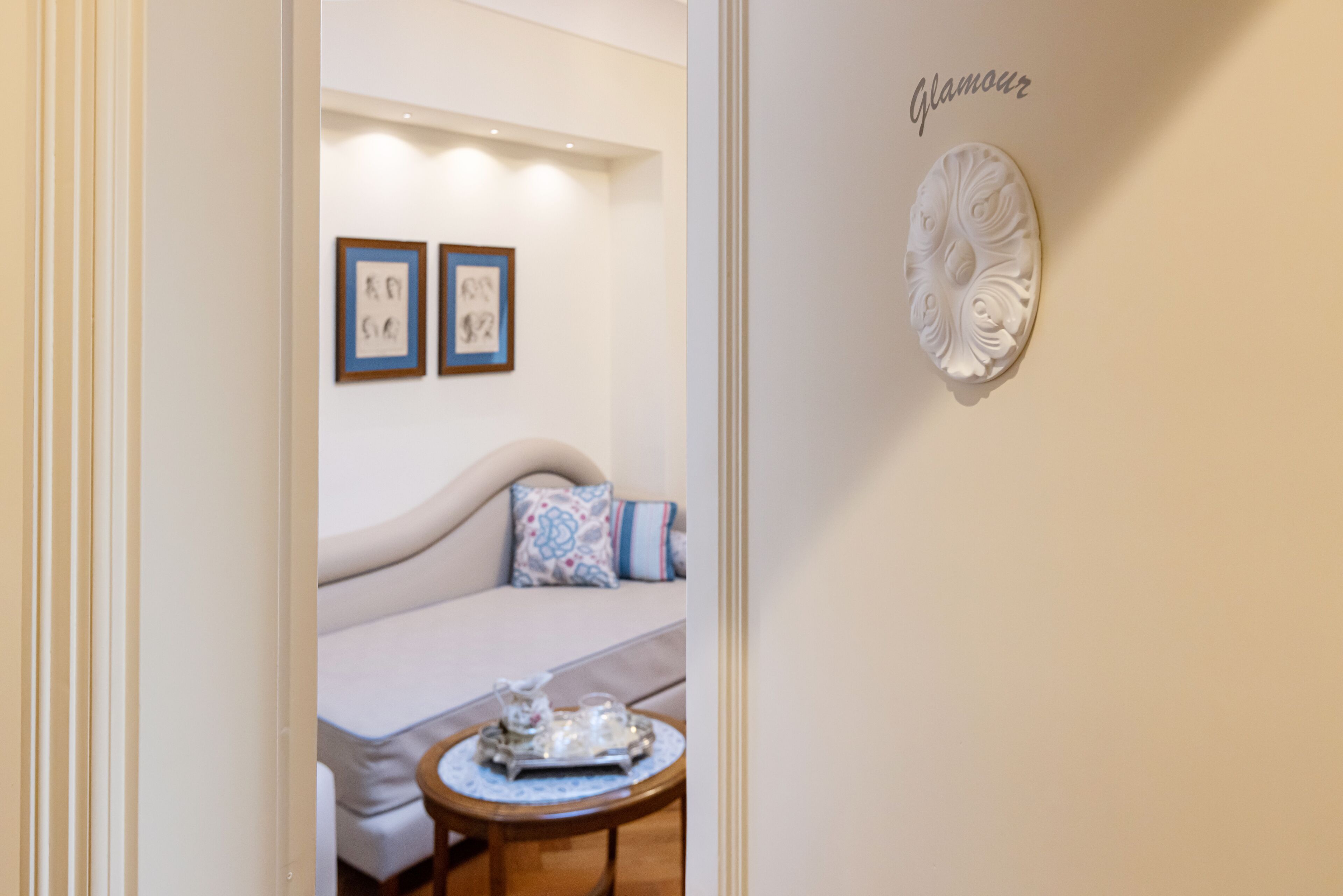 A cozy room with a sofa, a small round table with a tray, and two framed artworks on the wall.