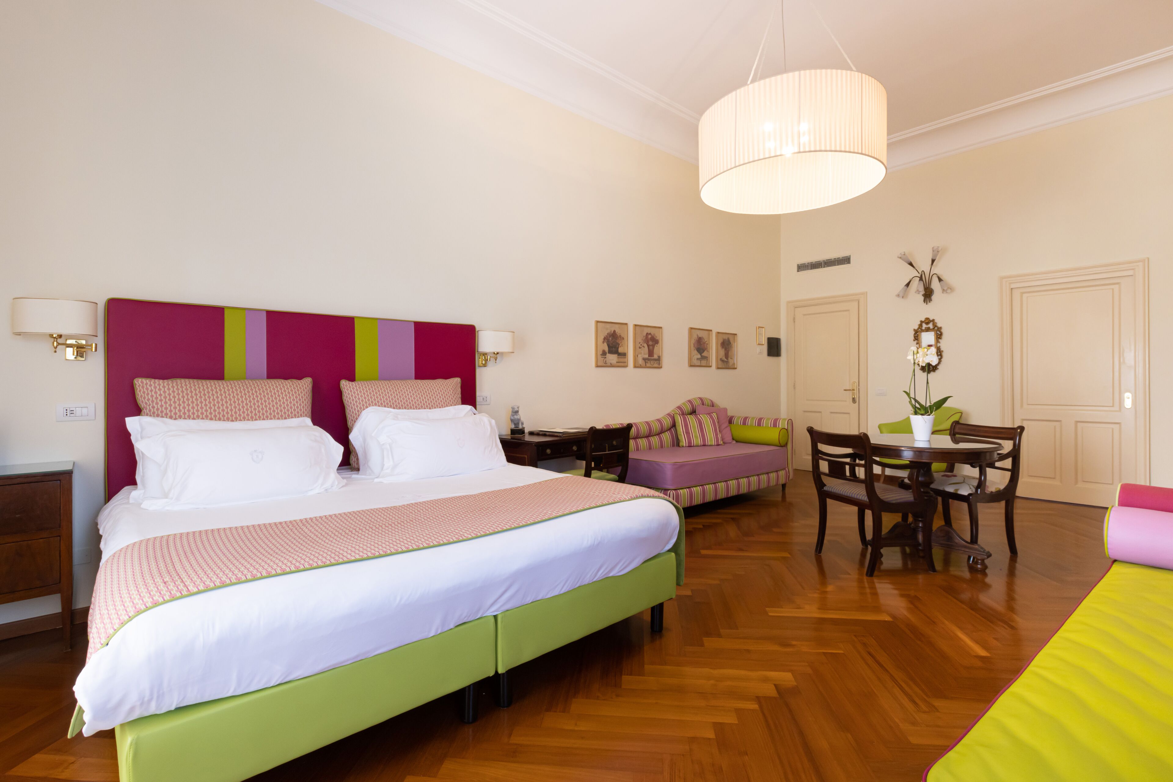 Ein Schlafzimmer mit einem großen Bett, einem grünen Sofa, einem Esstisch mit Stühlen und einer Pendelleuchte.