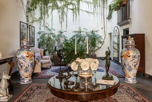 A room with a round glass table, large vases, a sofa, and a large window with plants.