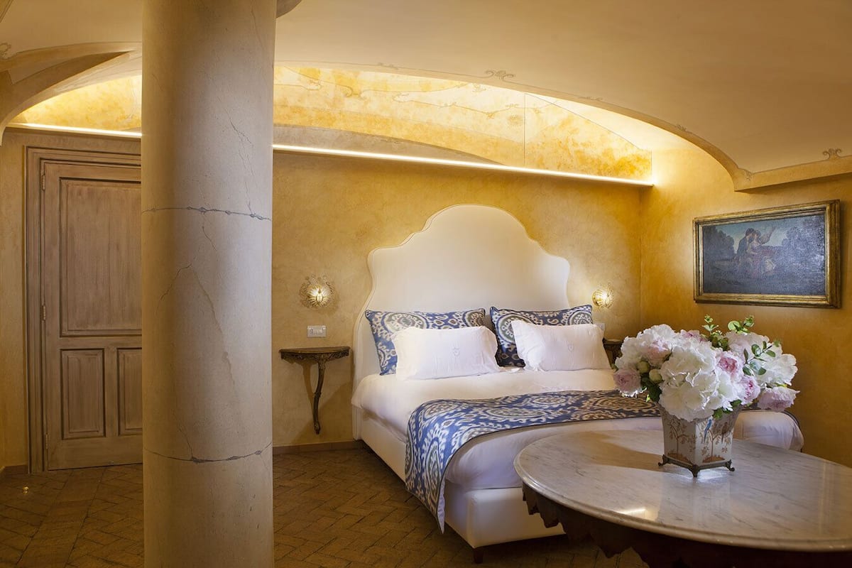 A bedroom with a large bed, a round table, and a vase of flowers.