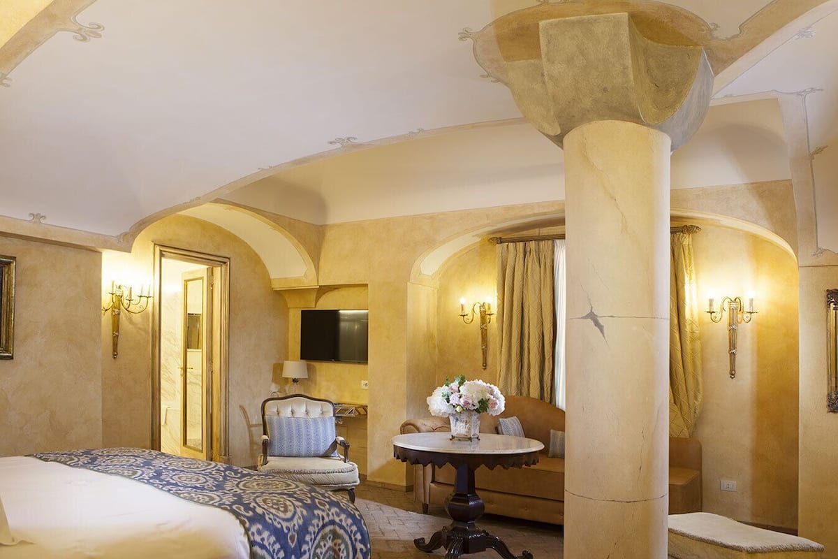 A hotel room with a bed, a chair, a table with flowers, and a TV.