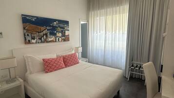 A hotel room with a large bed, a bedside table, a chair, a painting on the wall, and a window with curtains.
