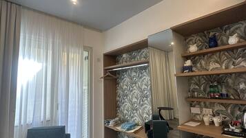 Una habitación de hotel moderna con un ventanal grande, una zona de estar, un armario y un tocador con estantes.