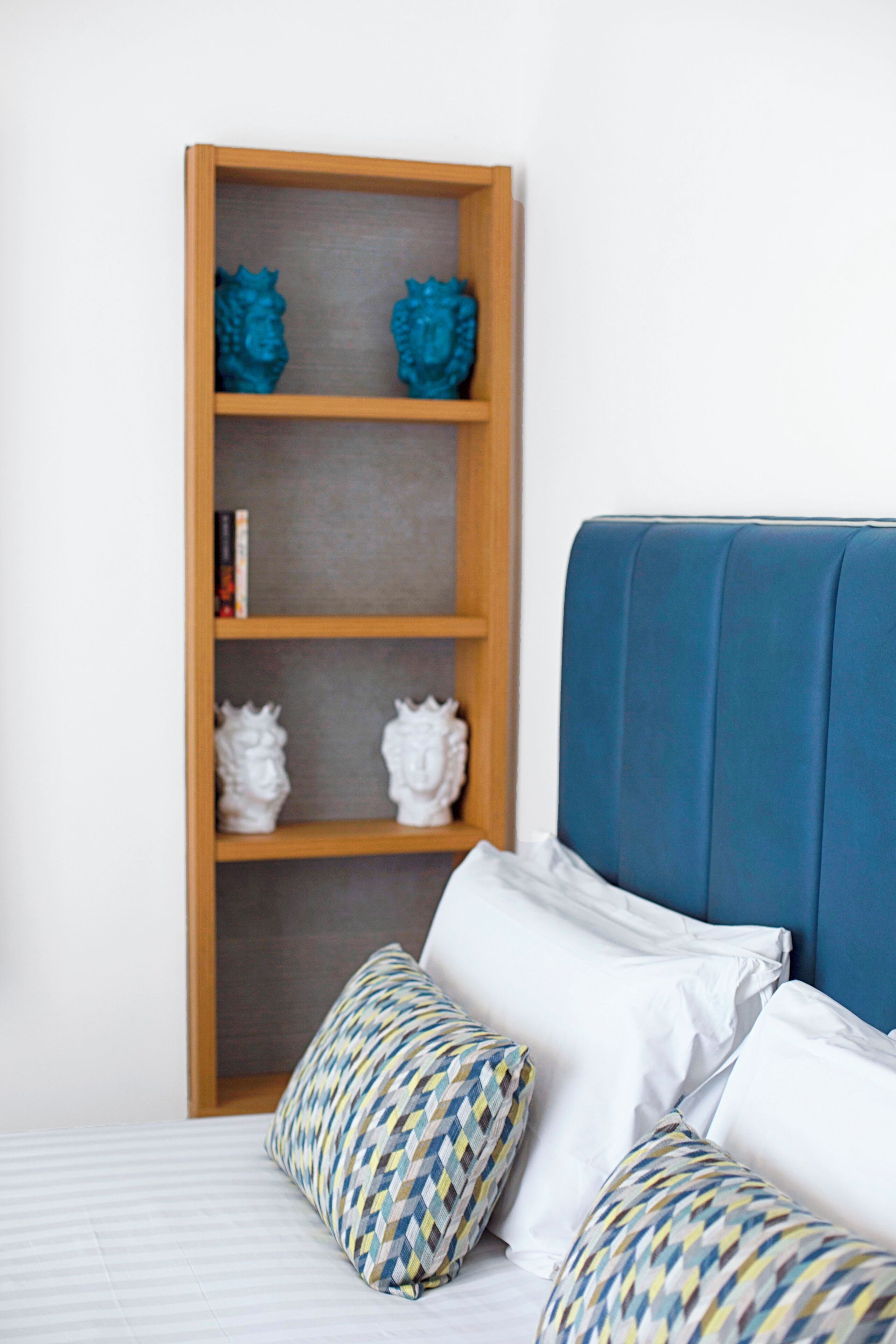 Une chambre à coucher avec un lit, une tête de lit bleue et une bibliothèque en bois agrémentée d’objets décoratifs.