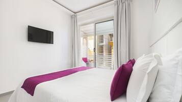 Habitación de hotel con cama, televisor y vista a un balcón con barandilla.