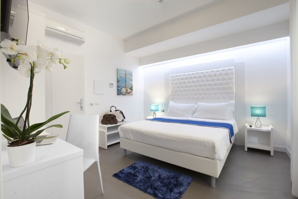 Un dormitorio moderno con una cama grande, mesitas de noche, un escritorio con una computadora portátil y una planta en maceta.