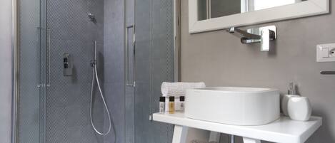Un baño moderno con ducha envuelta en vidrio, un lavamanos blanco y un espejo sobre él.