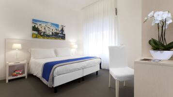 Habitación de hotel con cama, mesitas de noche, una silla, un escritorio, un cuadro y una planta en maceta.