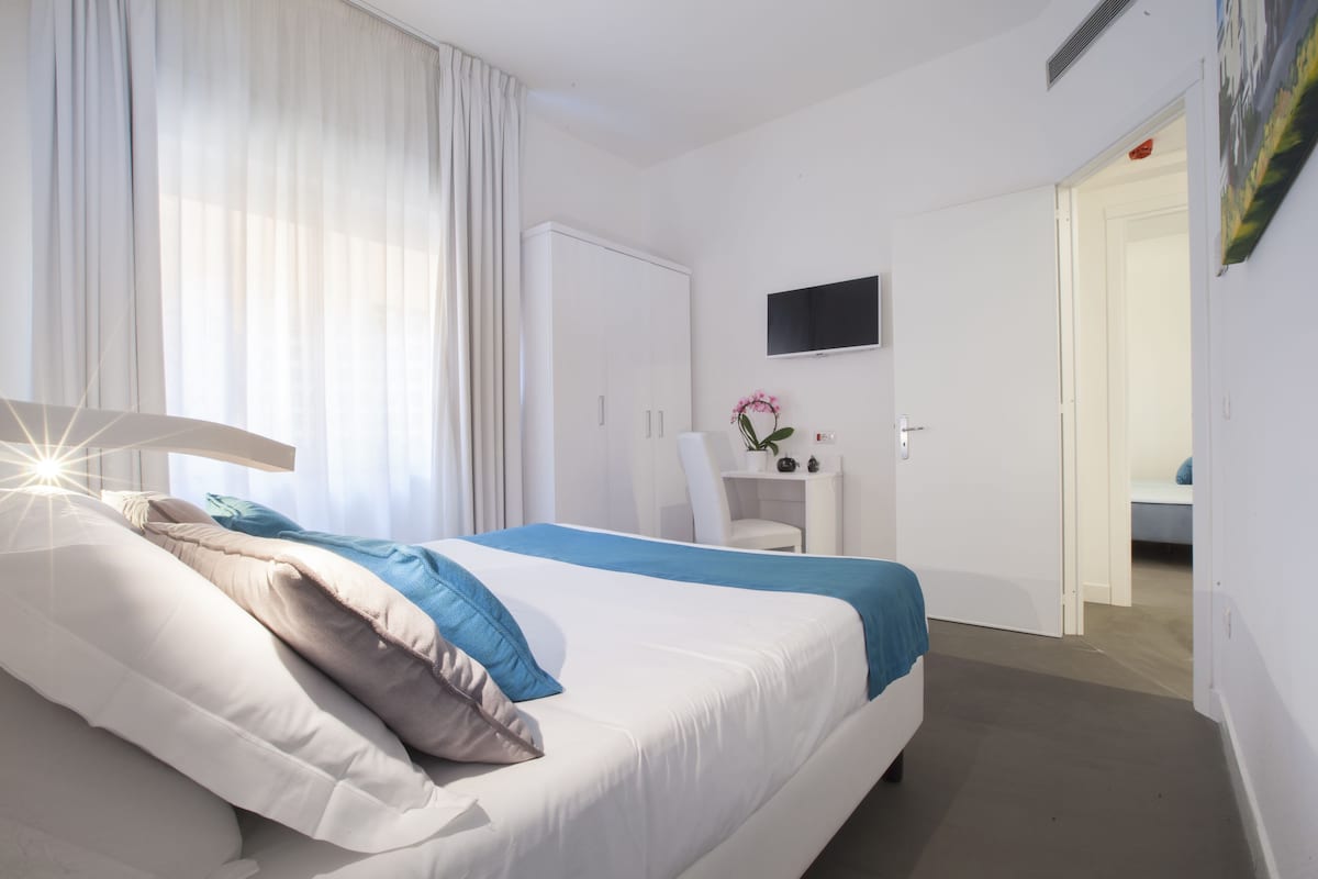 Habitación de hotel con cama, escritorio, silla, televisor y puerta que da a otra habitación.