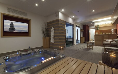 A modern spa room with a hot tub, wooden flooring, a wall-mounted TV, and a serene decor.