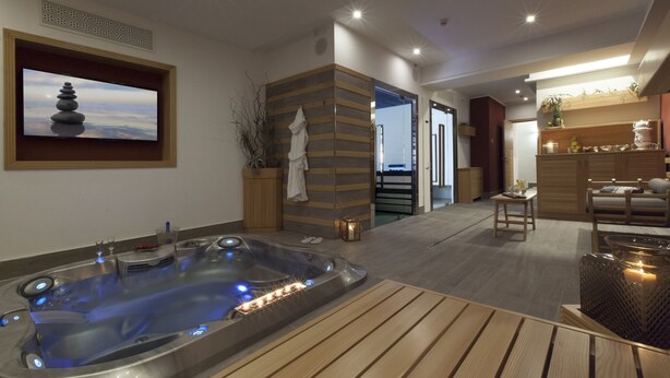Un spa moderno con bañera de hidromasaje, suelo de madera, televisor montado en la pared y una decoración tranquila.