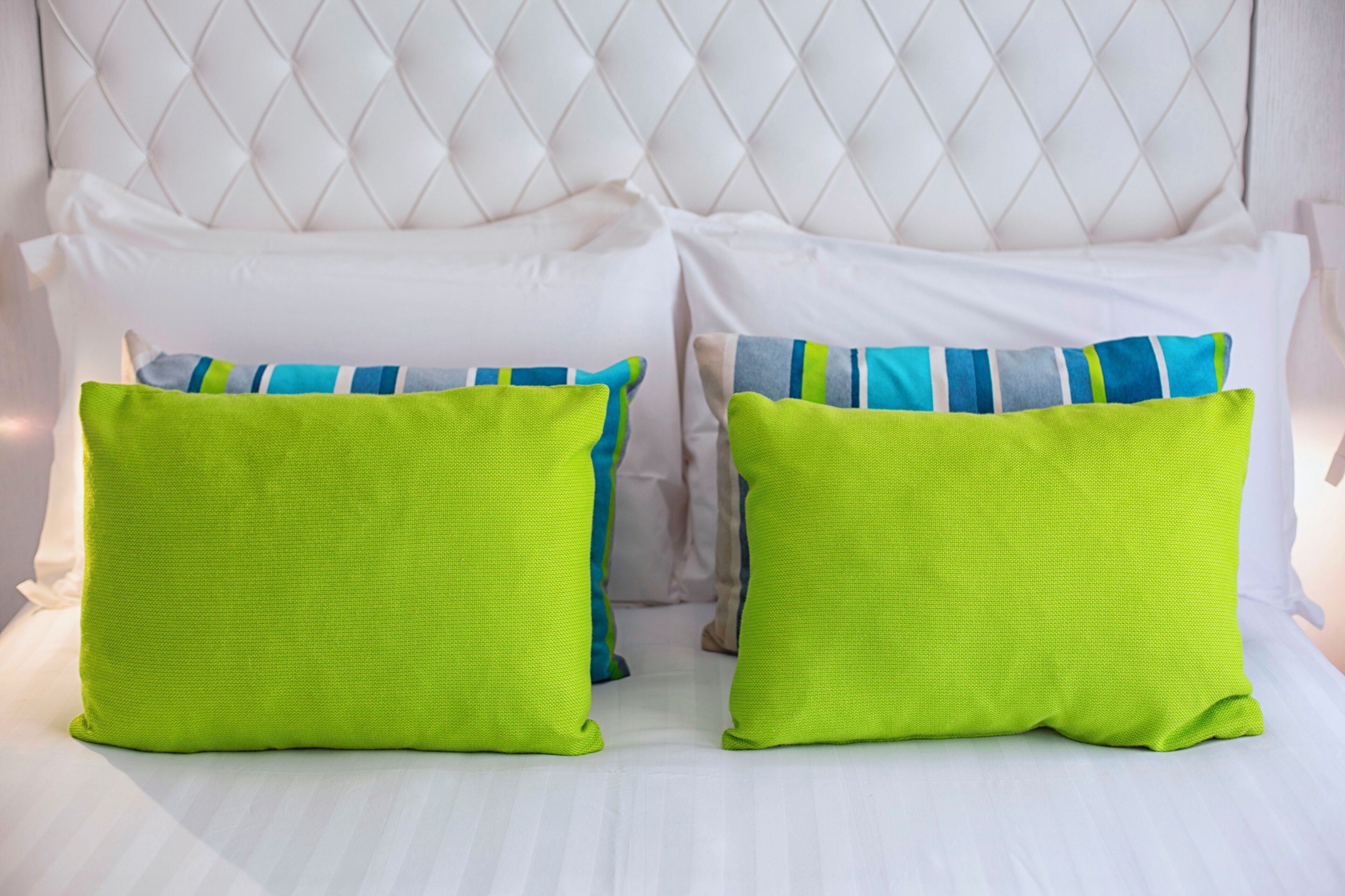 A bed with white bedding and two bright green pillows.