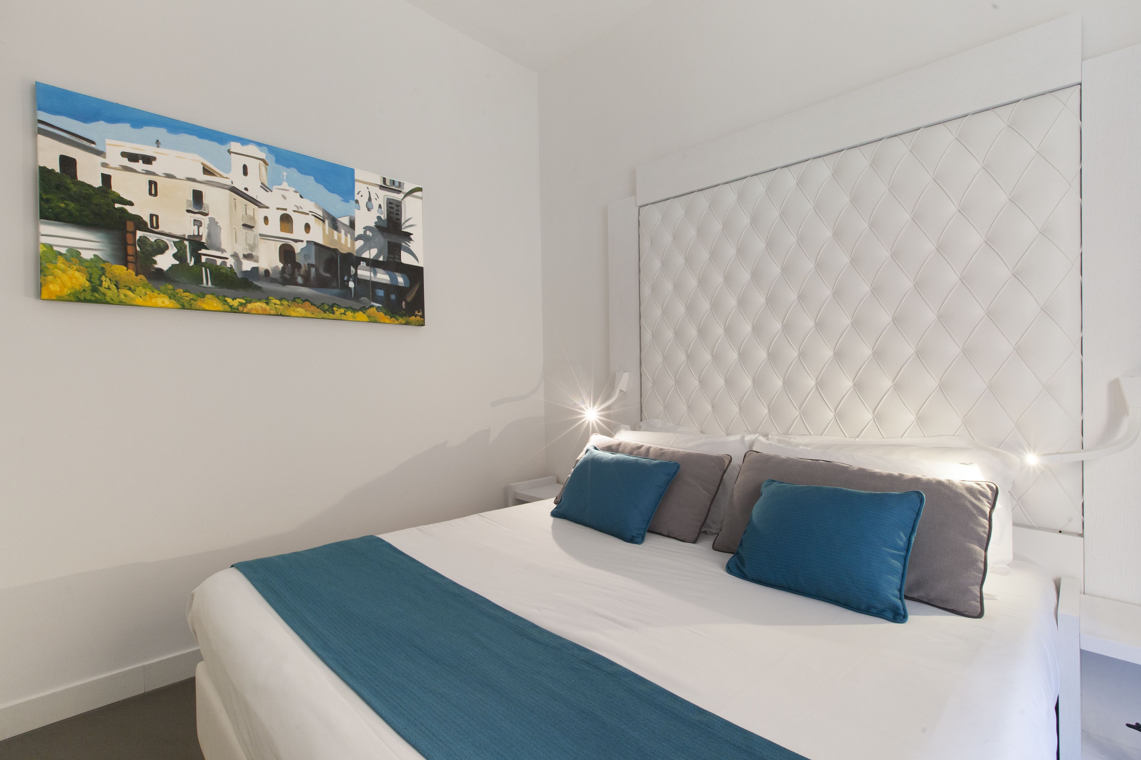 A bedroom with a bed, pillows, a headboard, a nightstand, and a painting on the wall.