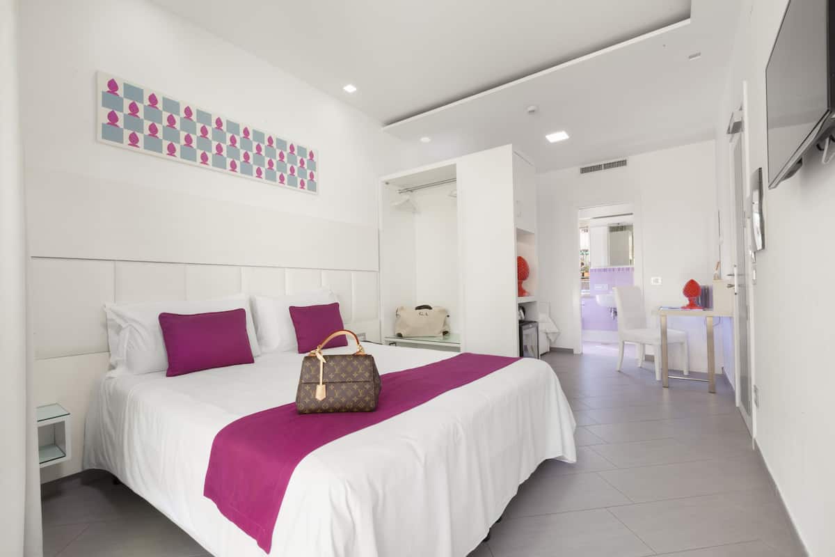 Una habitación de hotel moderna con una cama bien hecha, una mesita de noche pequeña y un espejo grande.