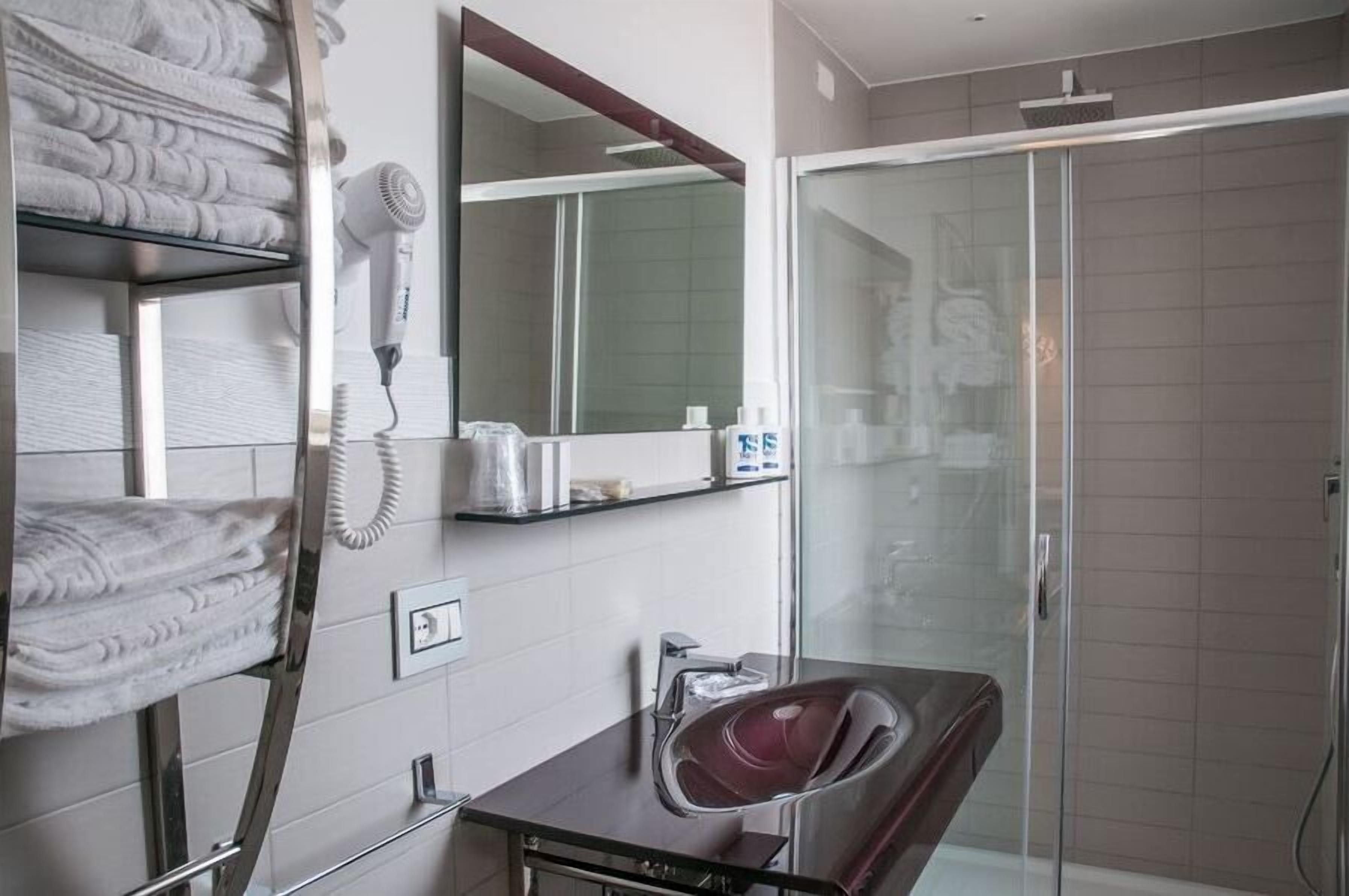 Une salle de bain moderne équipée d’un sèche-cheveux, d’un porte-serviettes, d’un miroir et d’une cabine de douche en verre.