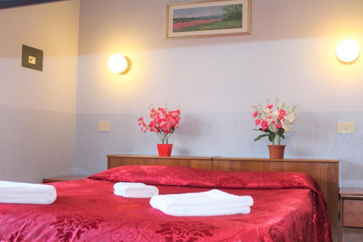 A hotel room with a bed, two wall-mounted lights, and two potted plants.