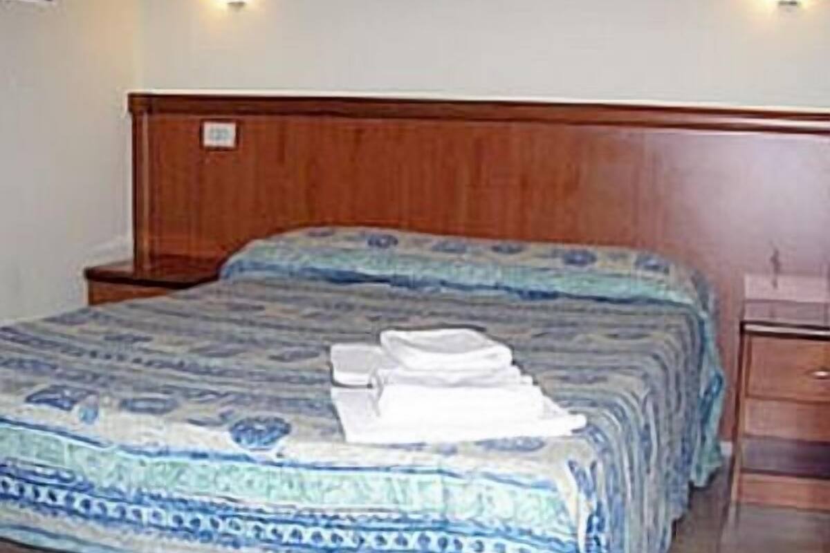 Et hotelværelse med sengegavl i træ, seng med mønstret dyne og to sengeborde med lamper.
