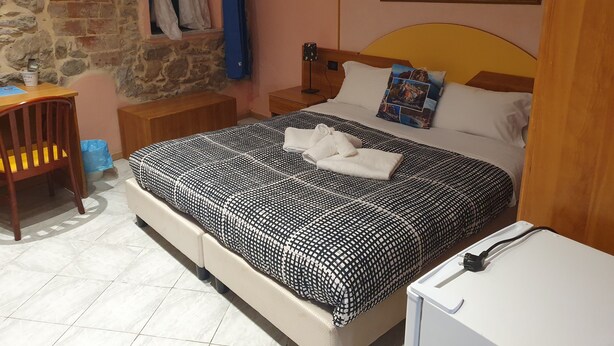 A hotel room with a bed, a desk, a chair, a nightstand, a lamp, and a painting on the wall. - Locanda dalla Compagnia (Riomaggiore)
