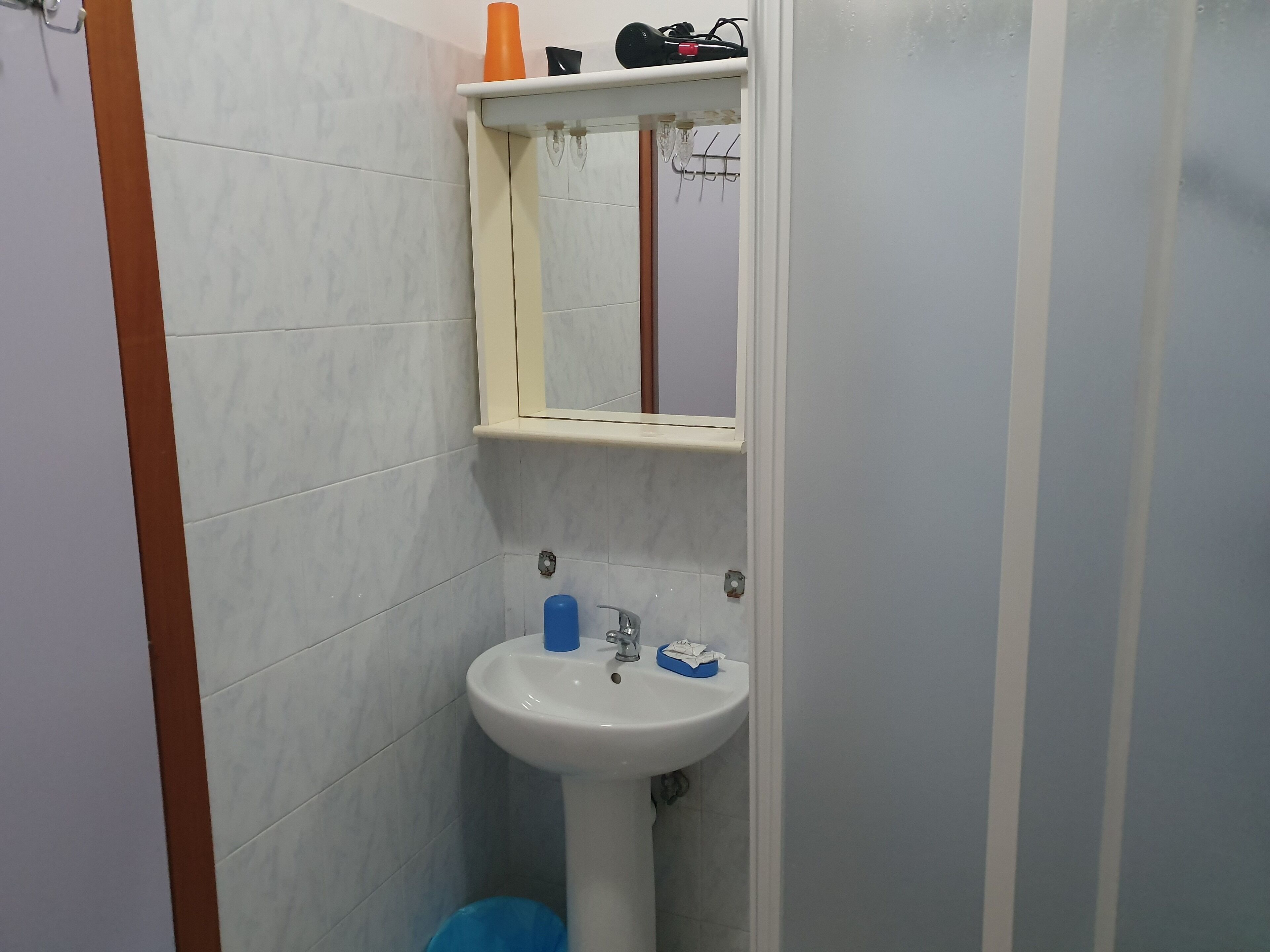 Un baño con lavamanos blanco, un espejo y un estante con artículos de aseo.