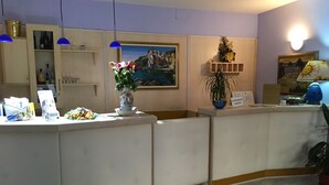 A reception area with a counter, a painting, and a potted plant. - Locanda dalla Compagnia (Riomaggiore)