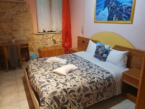 Un dormitorio con cama, un escritorio de madera, un muro de piedra y un cuadro.