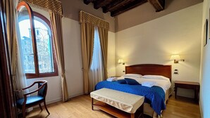 A bedroom with a wooden bed, a bench, a chair, and a window with curtains. - Locanda del Ghetto (Venice)