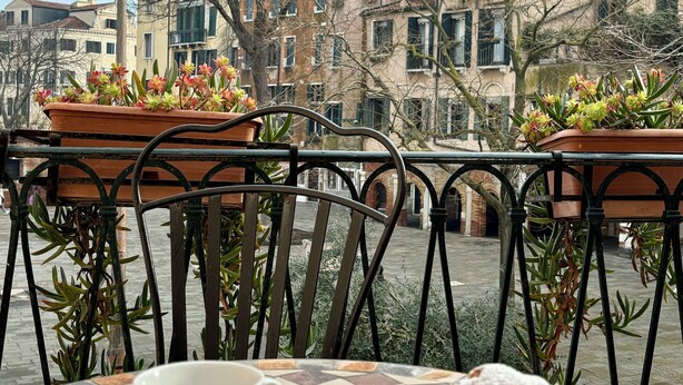 A table with a cup and a croissant, surrounded by metal chairs and potted plants. - Locanda del Ghetto (Venice)
