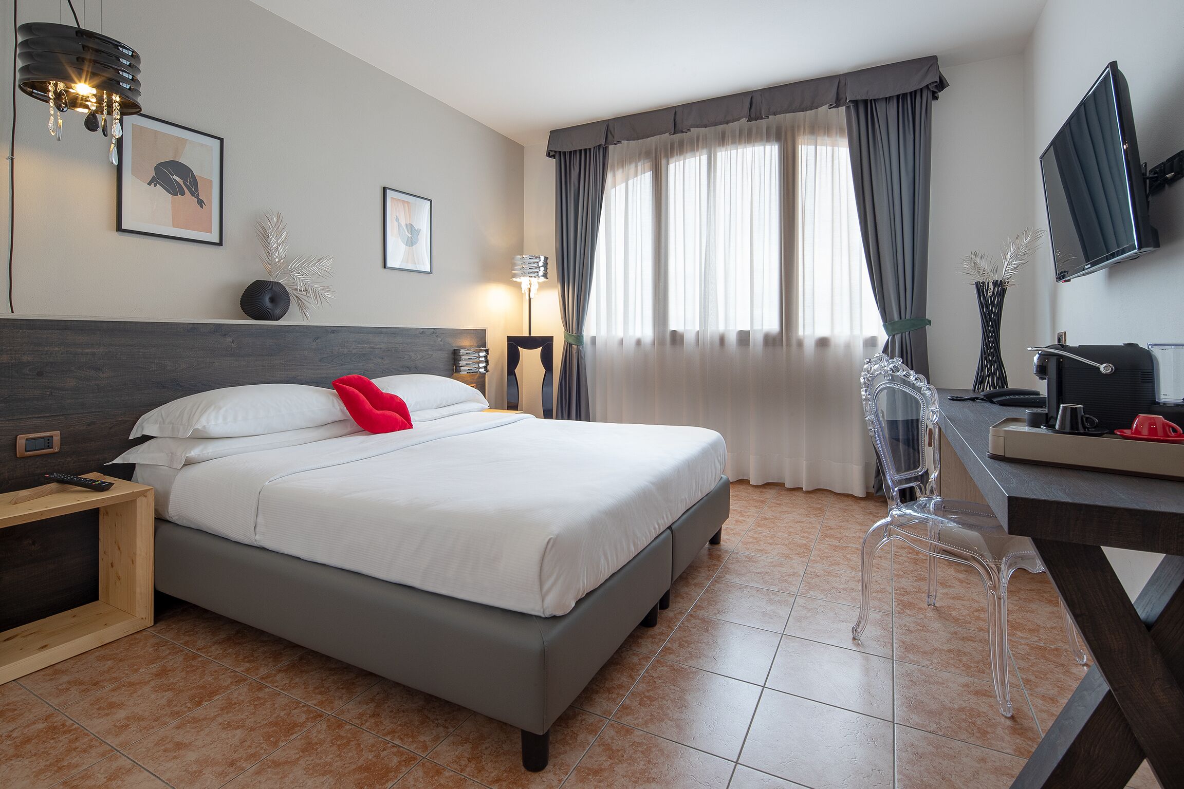 A modern hotel room with a large bed, a desk with a chair, a TV, and a window with curtains.