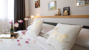 Una cama bien hecha con ropa de cama blanca y almohadas con letras doradas, un cabecero de madera y una mesita con un florero.