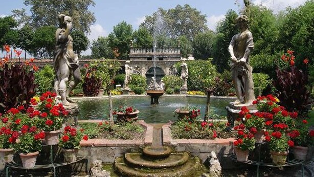 Ein Garten mit Statuen, einem Brunnen und einer Brücke.