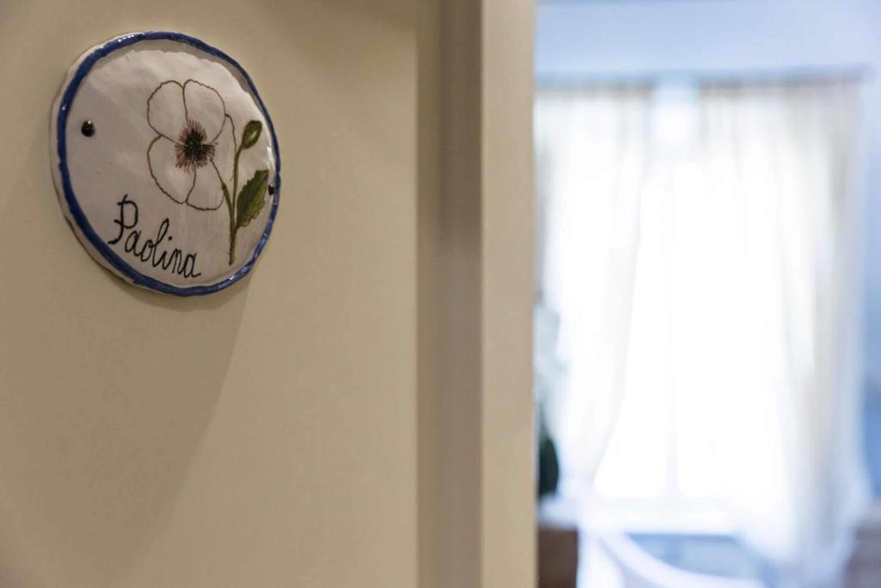 Una targa appesa al muro con un motivo floreale e il nome Paolina.