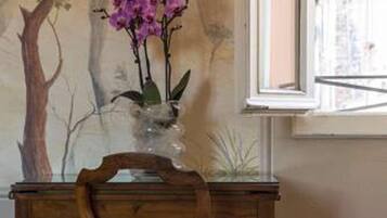 Una camera da letto con un letto, una sedia di legno, un tavolino con un vaso di fiori e un affresco sulla parete.