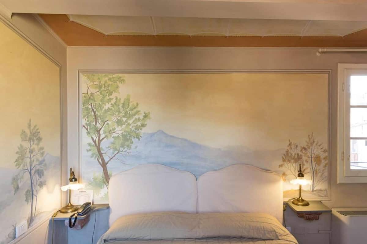 Un dormitorio con una cama centrada bajo un mural de paisaje montañoso. Hay dos mesitas de noche con lámparas.