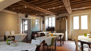 Un comedor con mesas dispuestas para comidas, vigas de madera en el techo y vista a la cocina al fondo.