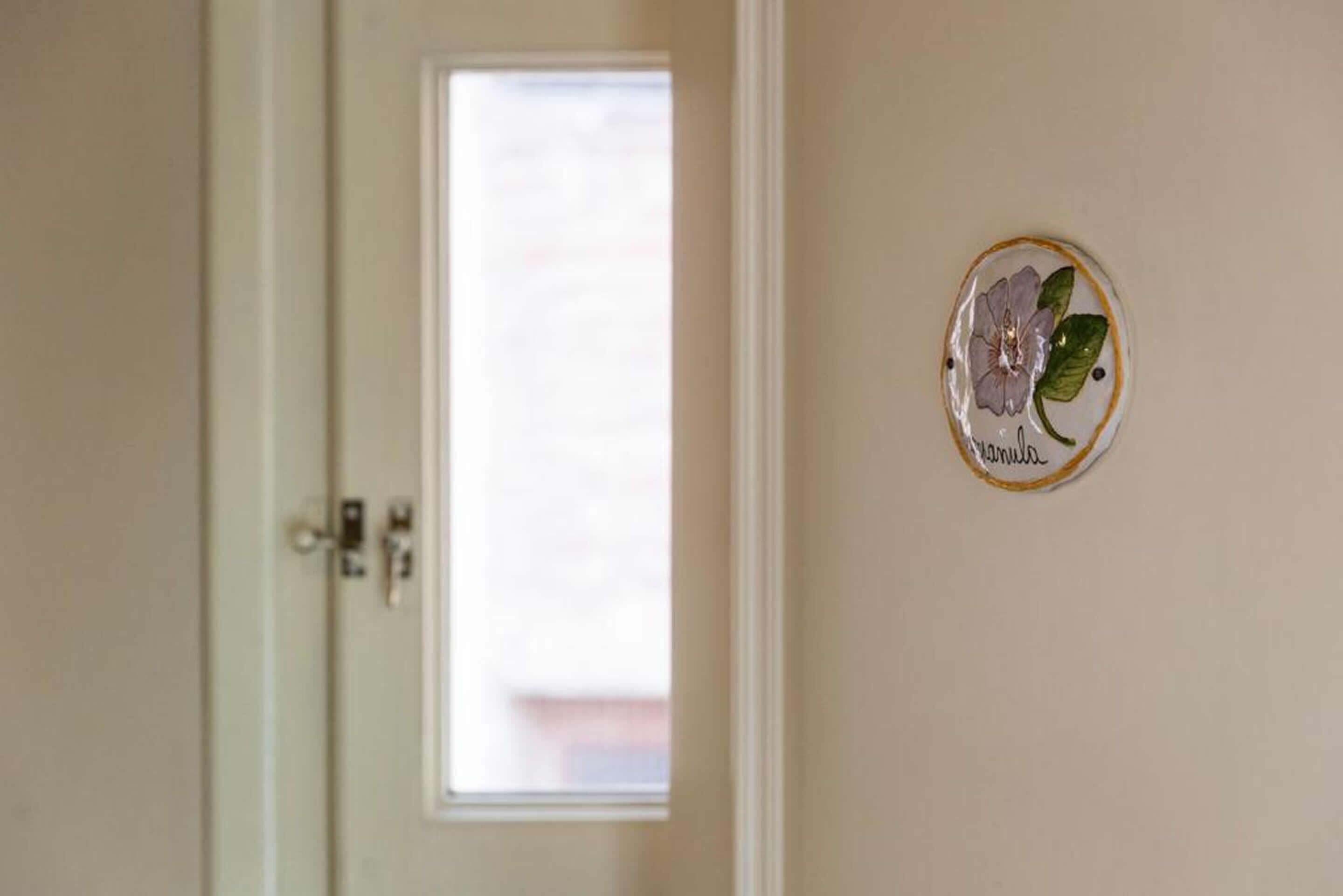 Una puerta con un ventanal, un plato decorativo en la pared con una flor y texto, y un pomo de puerta.