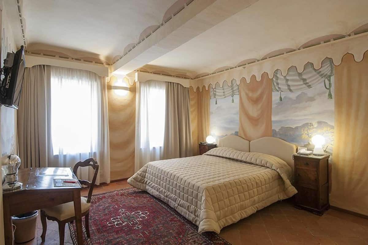 Un dormitorio con una cama, un escritorio y una silla. Hay cortinas en las ventanas y un cuadro en la pared.