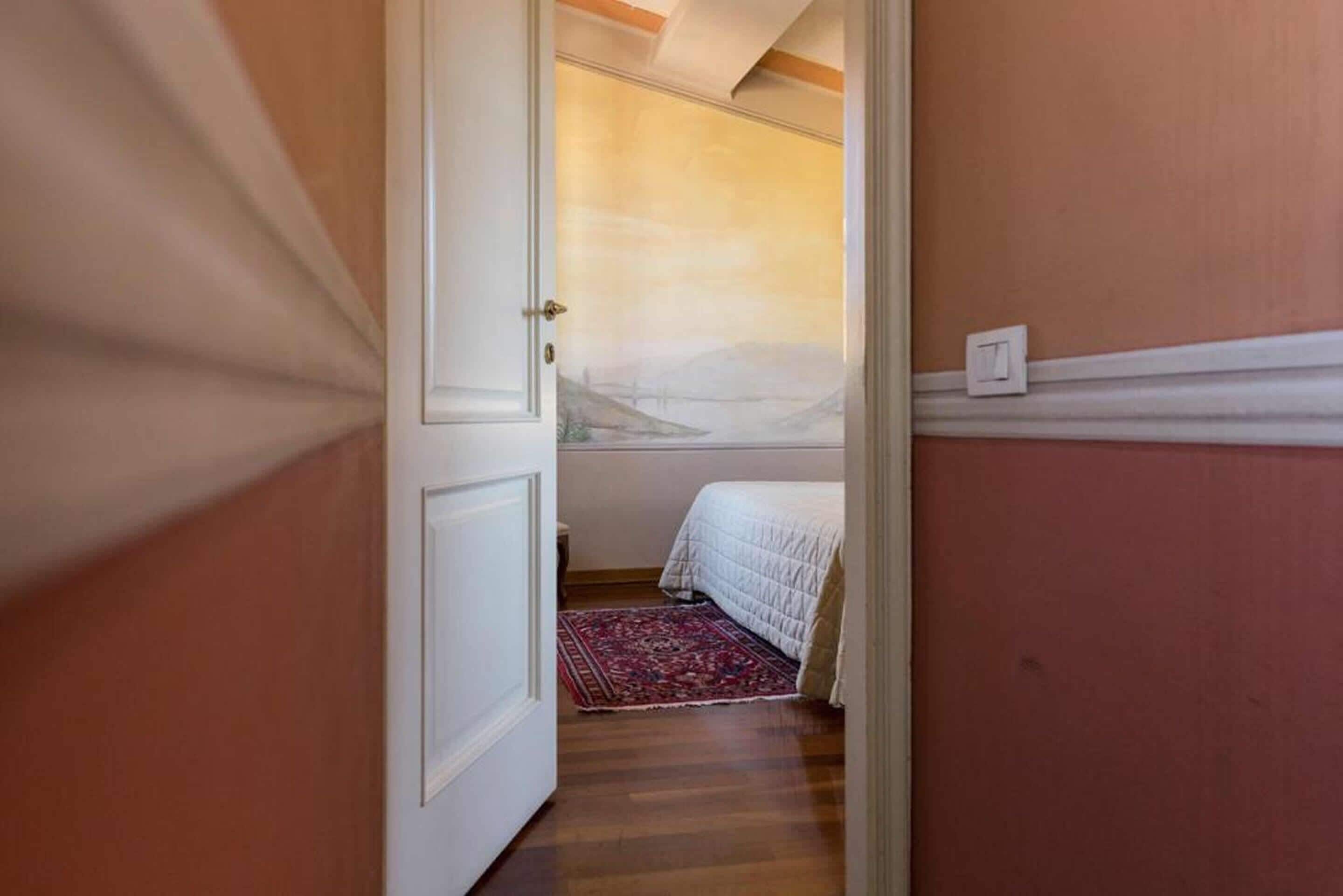Camera da letto con un letto, un tappeto rosso decorato e vista su un paesaggio attraverso una finestra.