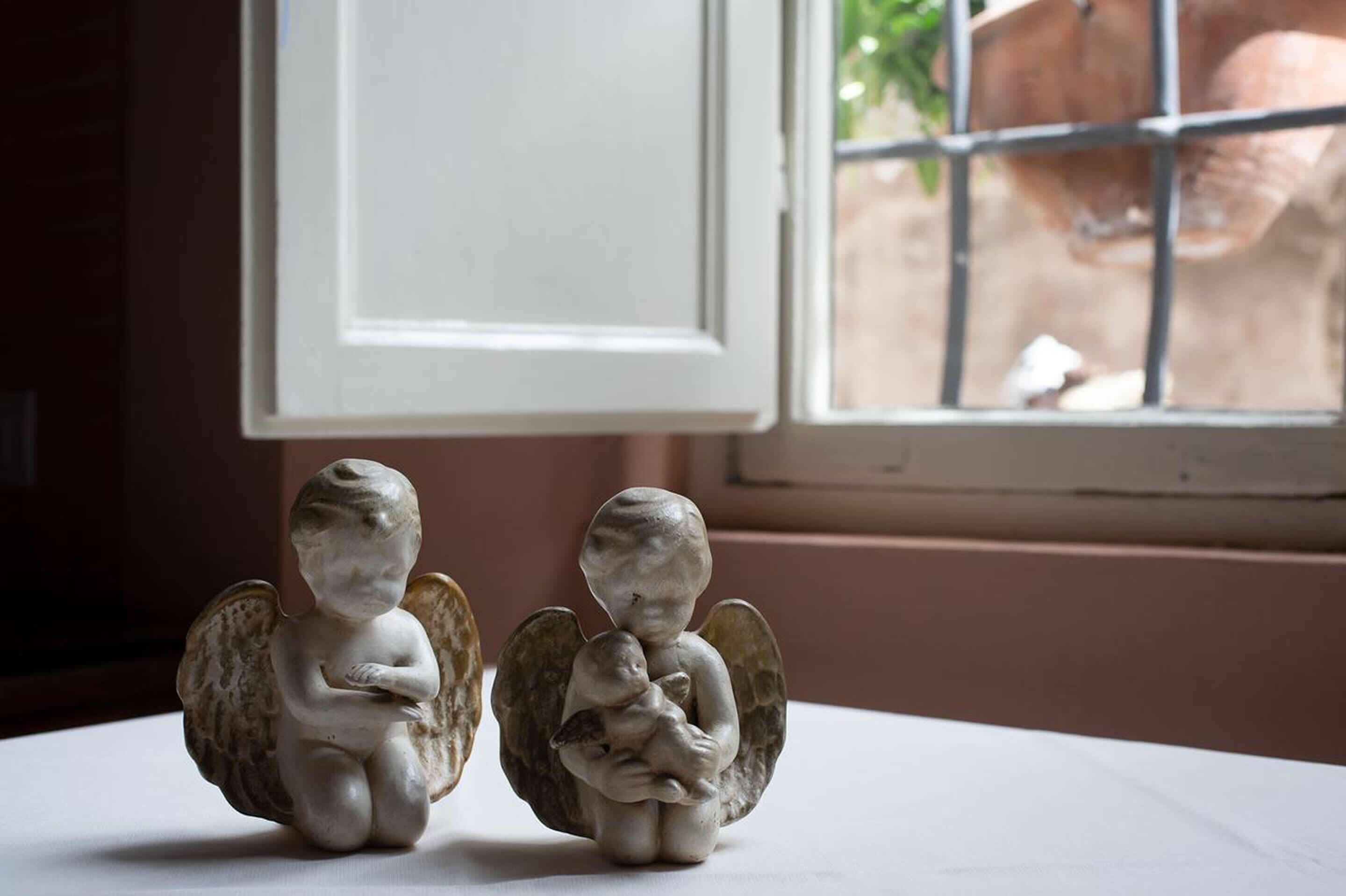 Due figurine di angeli su un tavolo vicino a una finestra con vista su un giardino.