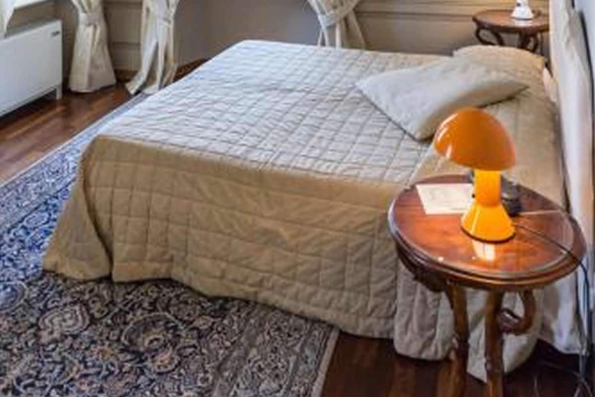 Un dormitorio con cama, mesita de noche, lámpara y ventana con cortinas.