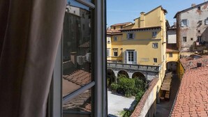 Vista desde una ventana sobre un patio con edificios, incluyendo un edificio amarillo con contraventanas y un puente de piedra.