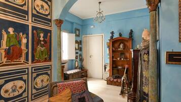 Una habitación con pared azul, una araña, un mueble de madera y un sofá estampado.