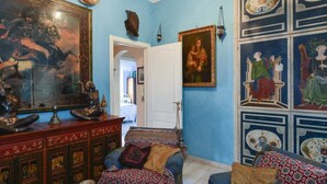 Une pièce avec un mur bleu, un grand tableau encadré, une armoire en bois et un lit avec une literie à motifs.