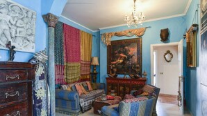 Une pièce avec un mur bleu, un lustre, un ensemble de meubles de salon, un buffet en bois et un tableau.