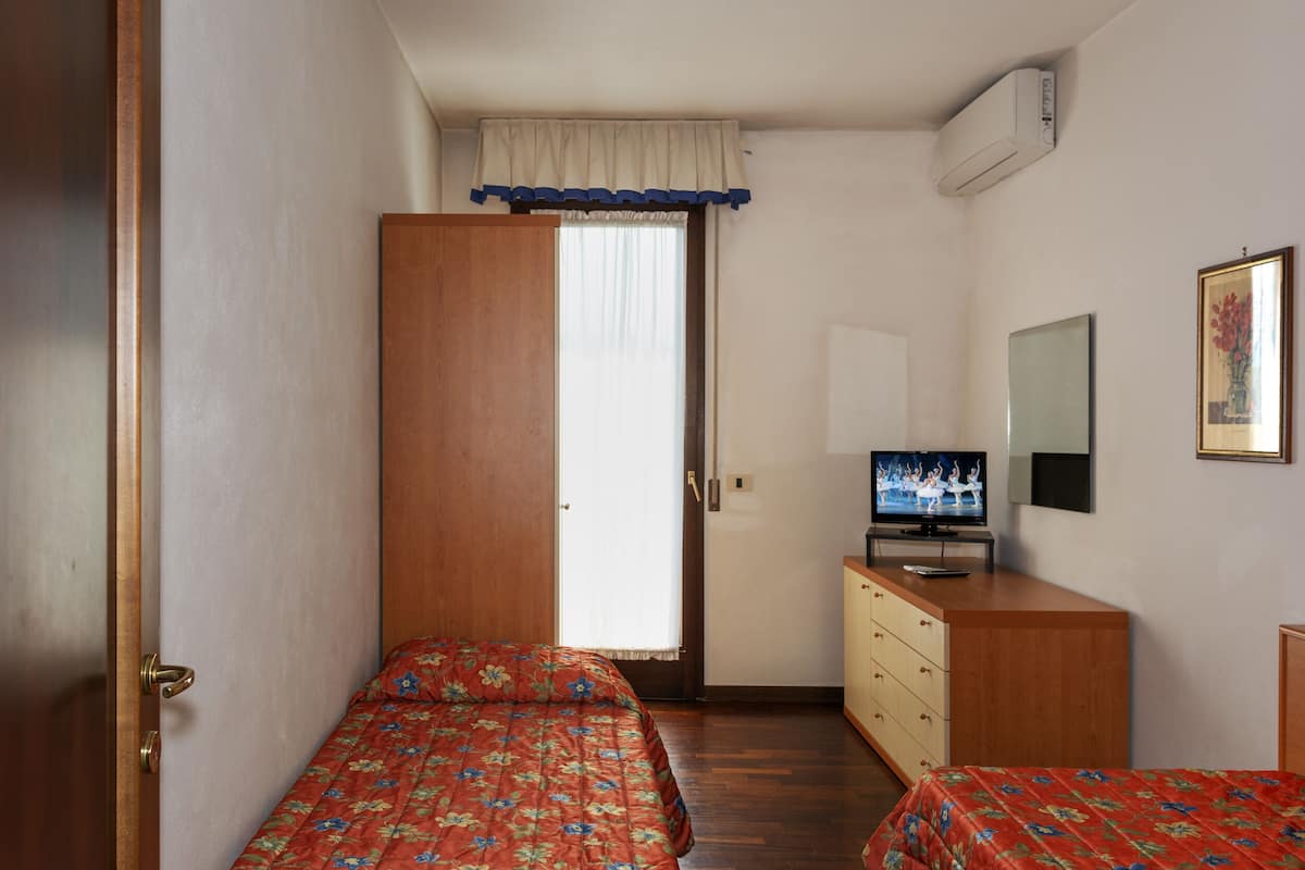 A bedroom with two single beds, a wooden wardrobe, a television on a dresser, and a window with curtains.